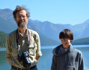 Man and son posing for phtoto with mountains and lake for backdrop