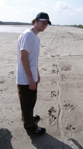 Student standing over tracks in the sand.