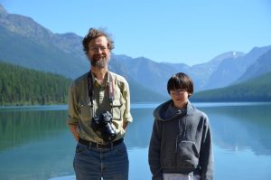 Man and son with lake and mountains as backdrop.